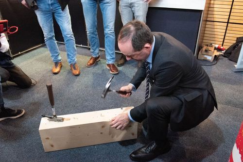 Wirtschaftsminister Hubert Aiwanger an einem Unternehmensstand beim Einschlagen eines Nagels.