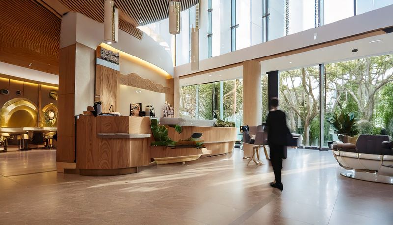Innenansicht einer Lobby eines Hotels mit einem Empfangstresen. Menschen gehen vorbei.