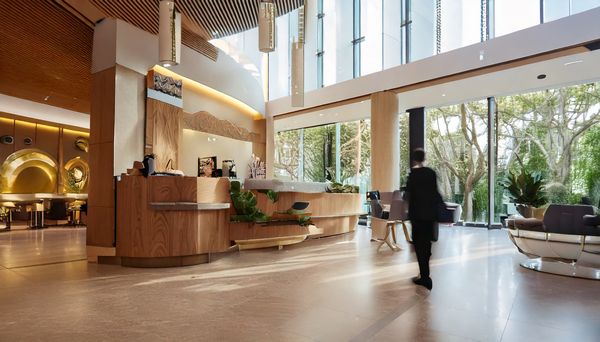 Innenansicht einer Lobby eines Hotels mit einem Empfangstresen. Menschen gehen vorbei.
