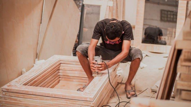 Ein junger Mann bearbeitet auf einer Baustelle Fensterrahmen mit einer Schleifmaschine.