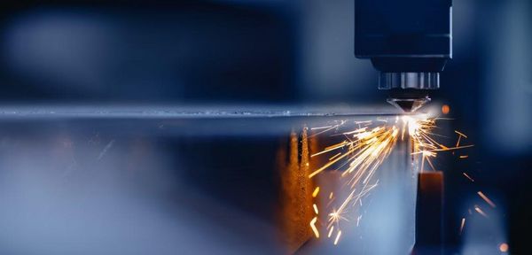 Beruf des Monats Metallbauer Nahaufnahme einer Laserschneidmaschine beim Schneiden von Metall – helle Funken fliegen.