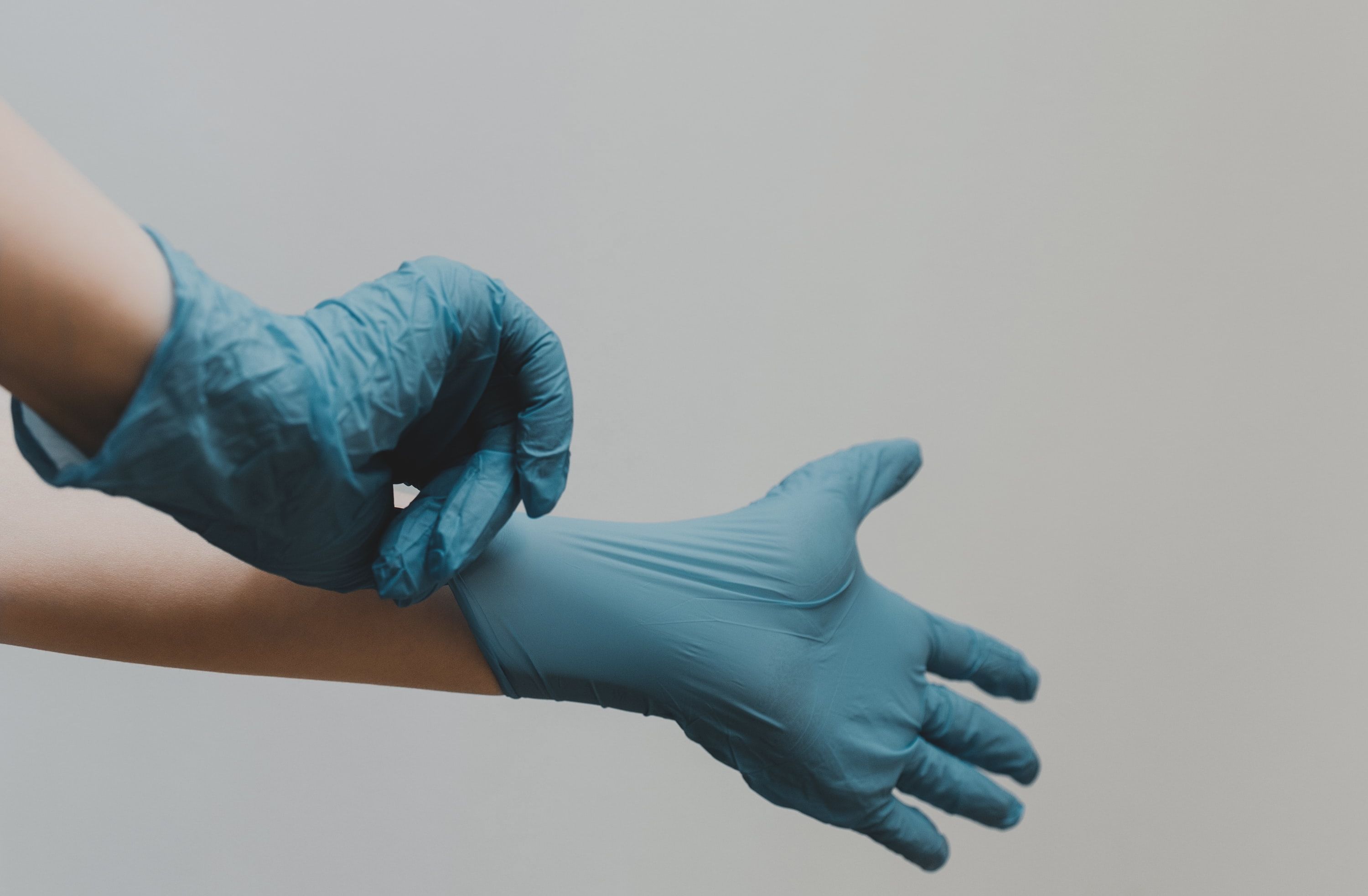 Als Pflegefachkraft ist Hygiene unerlässlich. Die Hände einer medizinischen Fachkraft beim Anziehen blauer Latexhandschuhe vor einem weißen Hintergrund.
