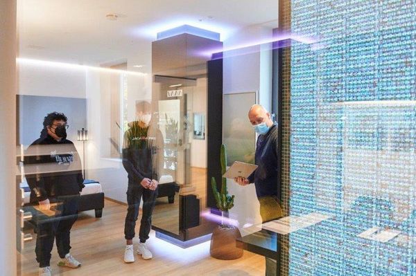 Der Geschäftsführer gibt den drei Praktikanten eine Führung durch den Smarthome-Showroom. Rechts leuchtet eine LED-Wand