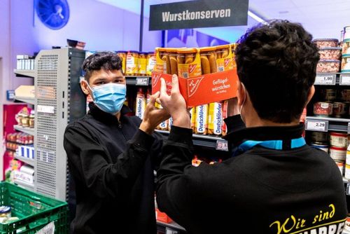 Zwei Praktikanten beim Auffüllen der Warenregale in einem Supermarkt.