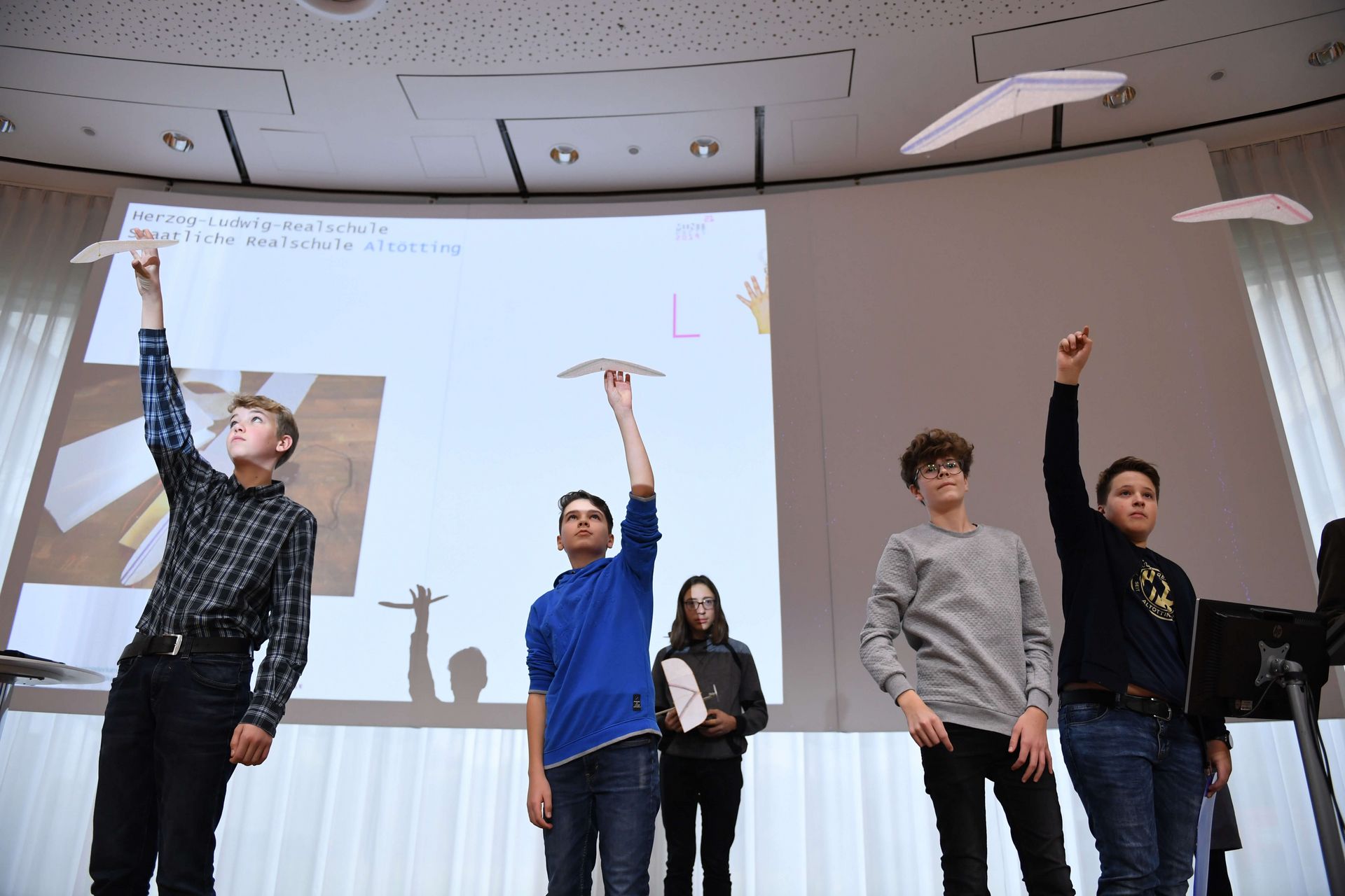 Schüler auf einer Bühne halten Papierflieger in die Luft.