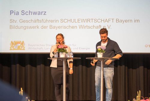 Pia Schwarz, Stv. Geschäftsführerin von SCHULEWIRTSCHAFT Bayern begrüßt auf der Bühne die anwesenden Gäste.