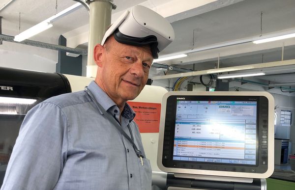 Wolfgang Böhm, Diehl Ausbildungsleiter, steht an einer Maschine und trägt eine VR Brille auf dem Kopf.