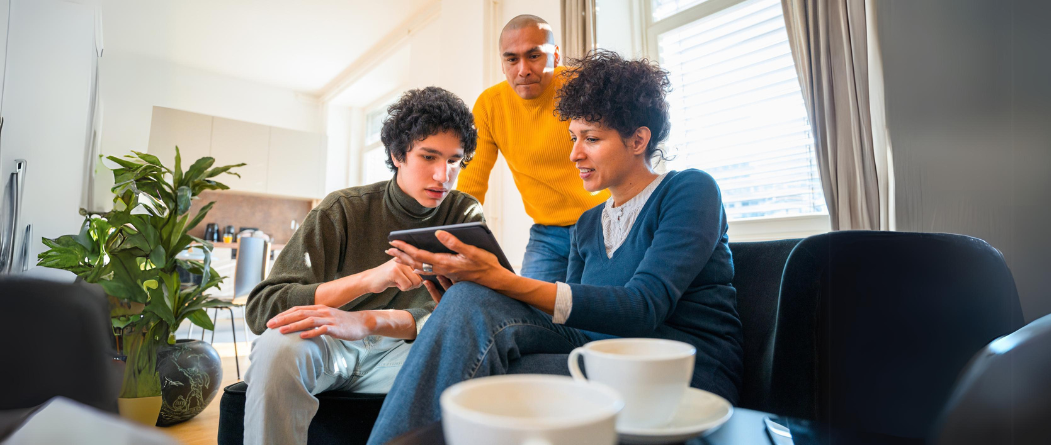 Drei Personen besprechen auf einem Tablet etwas im Wohnzimmer, Fokus auf Tablet-Nutzung