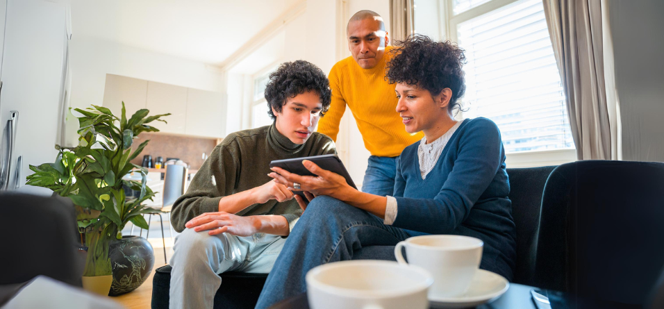 Drei Personen besprechen auf einem Tablet etwas im Wohnzimmer, Fokus auf Tablet-Nutzung