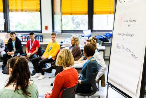 Eine Workshopgruppe sitzt im Stuhlkreis. Im Vordergrund ein Flipchart.