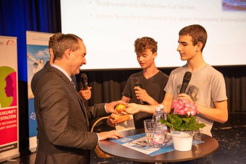 Ein Schüler überreicht dem Bayerischen Wirtschaftsminister Hubert Aiwanger einen Apfel.