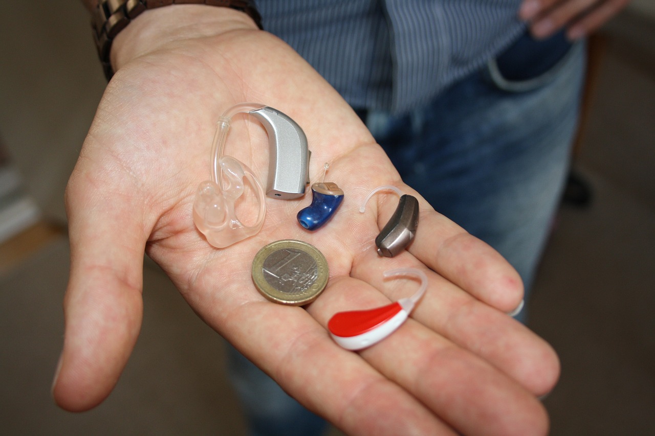 Verschiedene Hörgeräte auf einer Handfläche im Vergleich zu einer 1 Euro Münze.