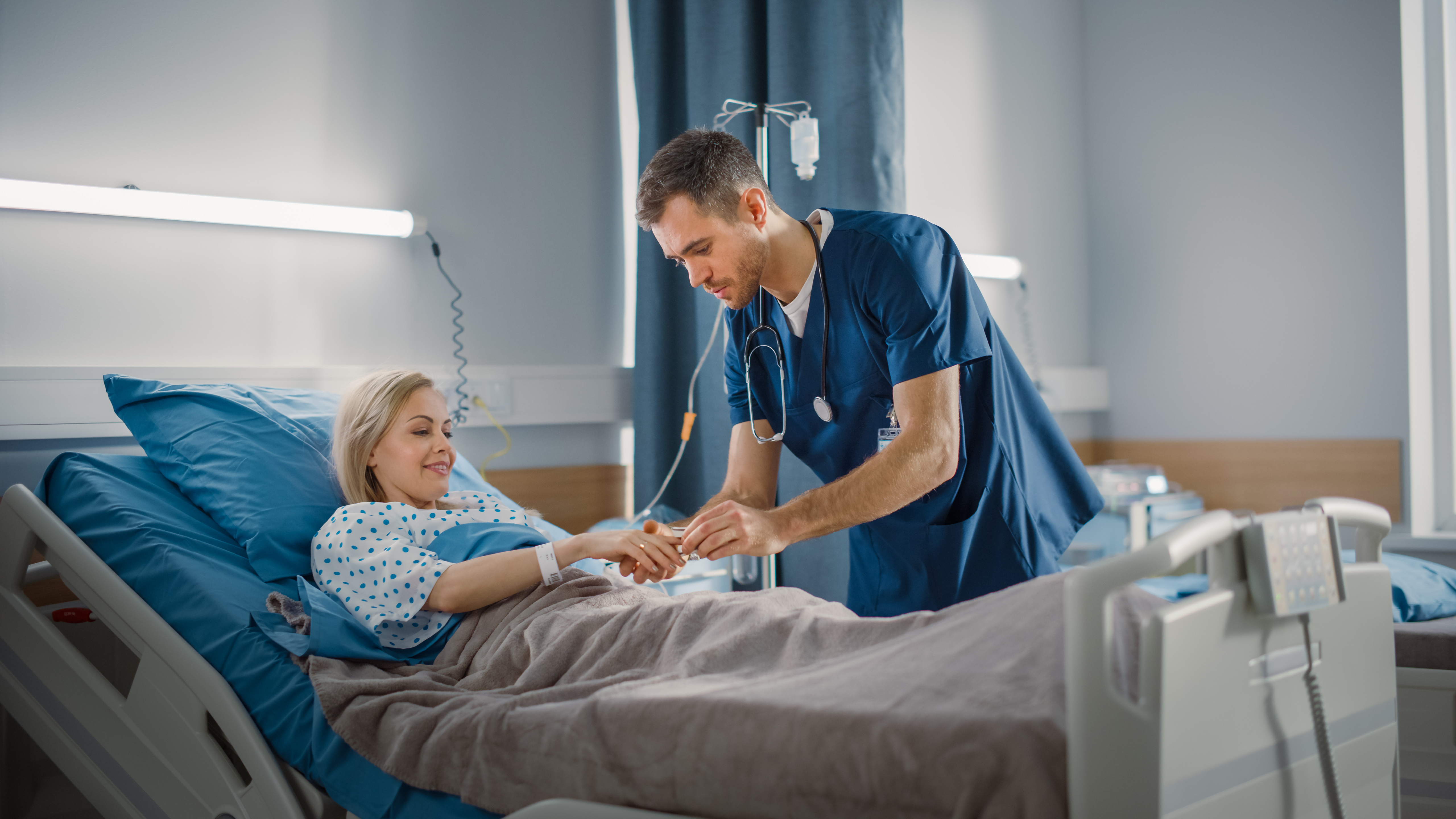 Ein junger Krankenpfleger beugt sich über das Bett einer Patientin