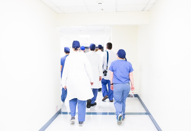 OTA_Medizin_sprungbrett Eine Gruppe Menschen in blauer OP-Kleidung geht durch einen blauen Gang