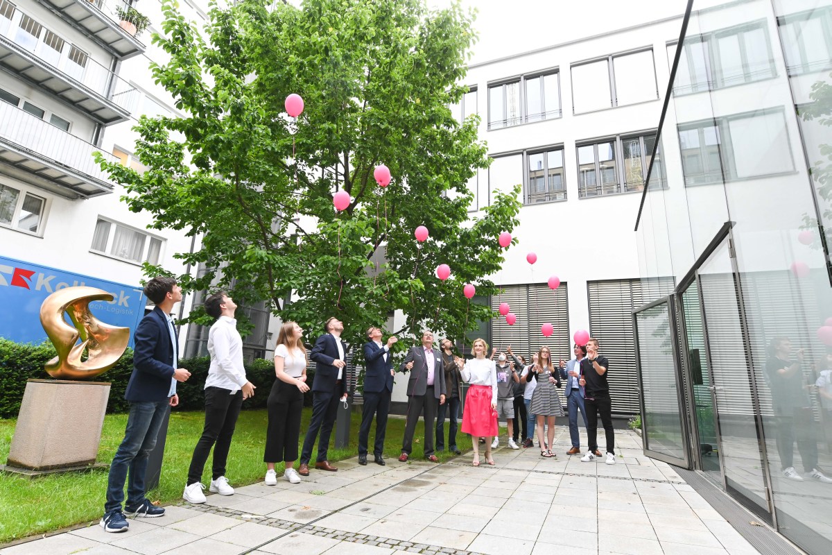 Eine Gruppe Erwachsener und Jugendlicher lassen in einem Innenhof Ballons in die Höhe steigen.