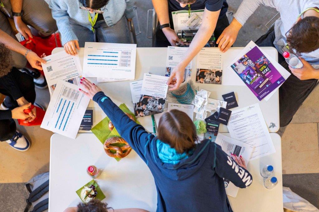 Schüler und Unternehmensvertreter im Gespräch beim sprungbrett SPEED DATING – Tisch mit Infomaterial, Getränken und Namensschildern.