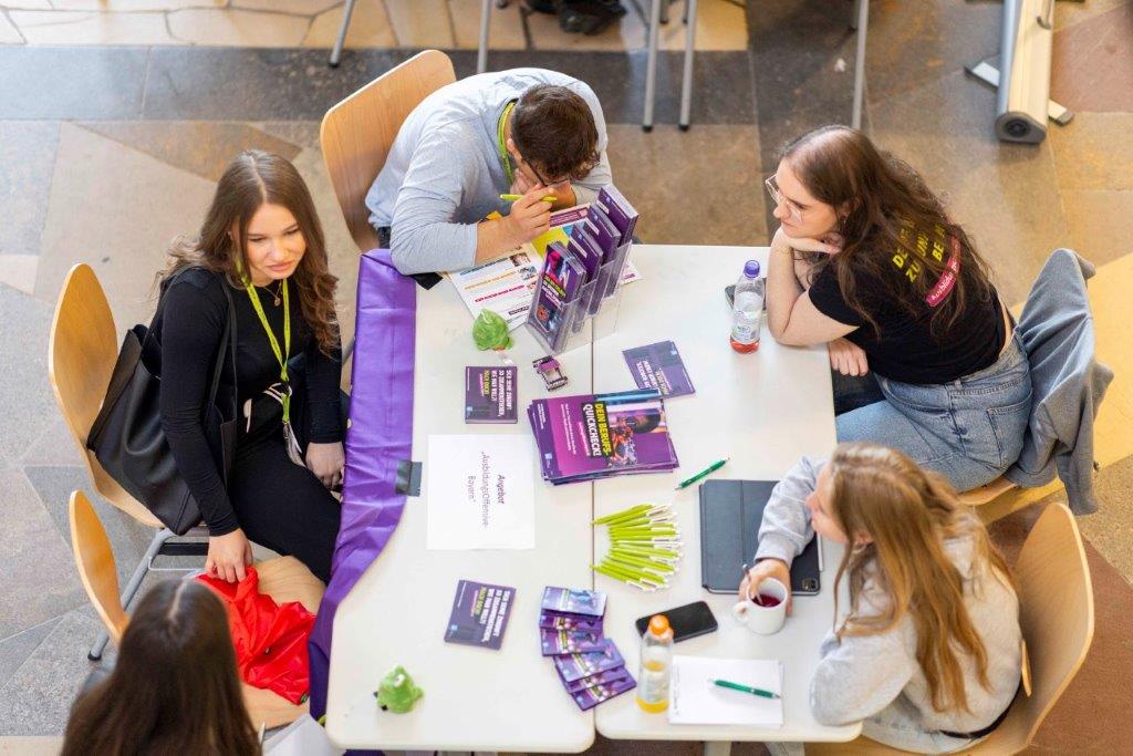 Fünf Personen am Tisch mit Flyern, Stiften, Wasserflasche und Froschfiguren – Szene vom sprungbrett SPEED DATING in Nürnberg.