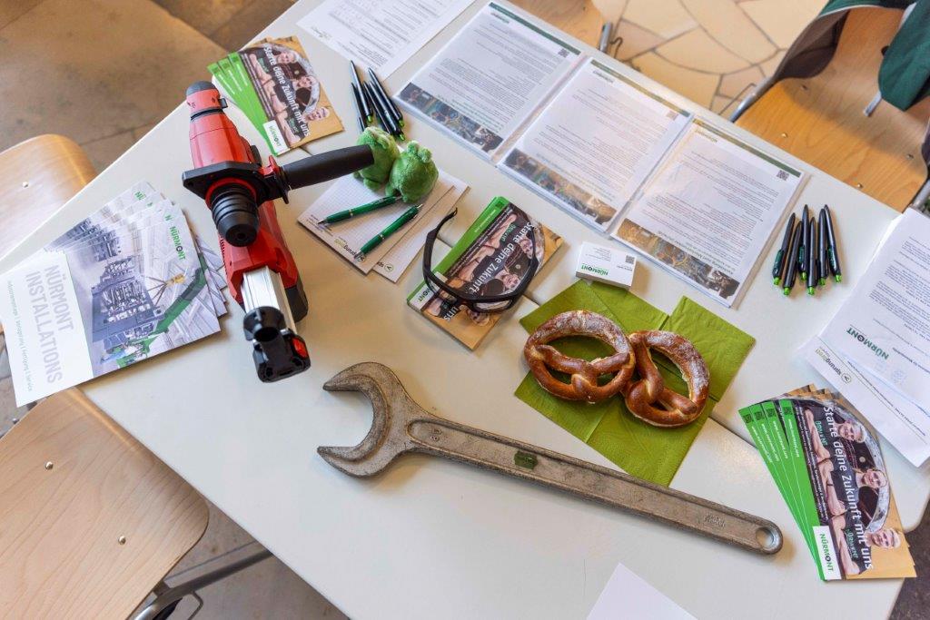 Tisch mit großem Schraubenschlüssel, Elektrowerkzeug, Flyern, Stiften und zwei Brezeln – Szene vom sprungbrett SPEED DATING in Nürnberg.