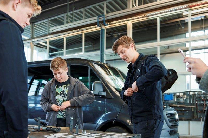 Drei junge Männer stehen um eine Werkbank in der Werkstatt und bearbeiten Kleinteile.